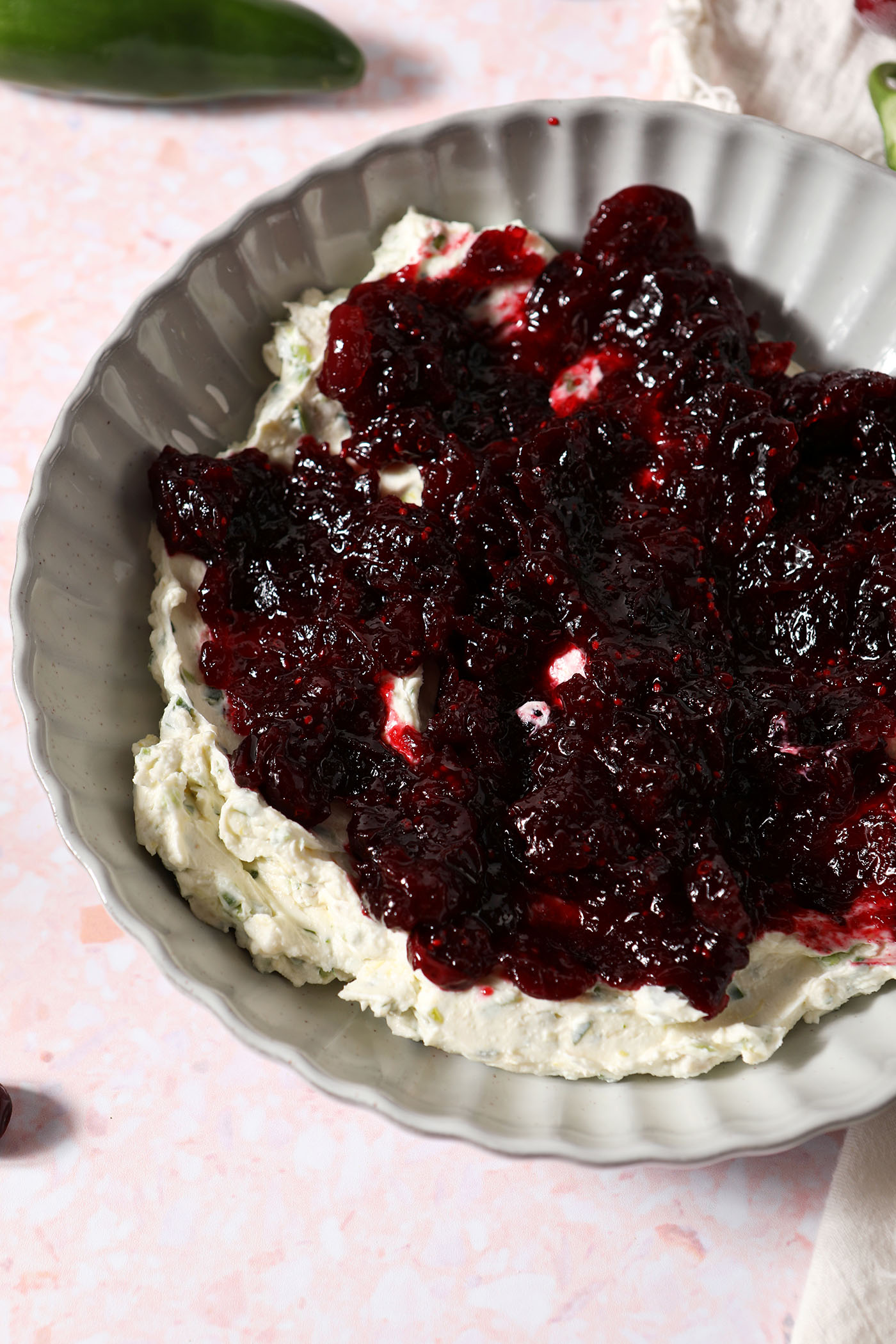 Cranberry sauce on top of jalapeño cream cheese in a grey scalloped bowl on a pink surface