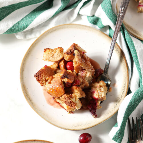 Overhead image of a plate of cranberry French toast casserole with a fork next to a green and white striped linen
