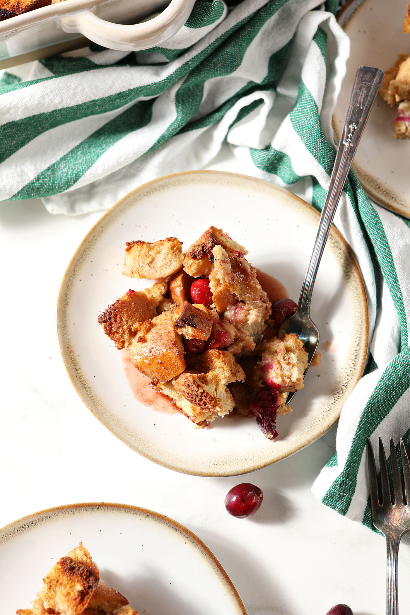 Overhead image of a plate of cranberry French toast casserole with a fork next to a green and white striped linen