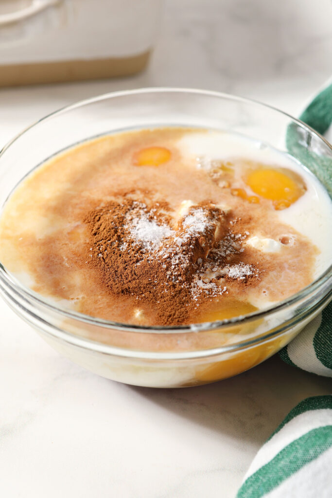 Custard ingredients in a glass bowl before mixing next to a green and white striped linen