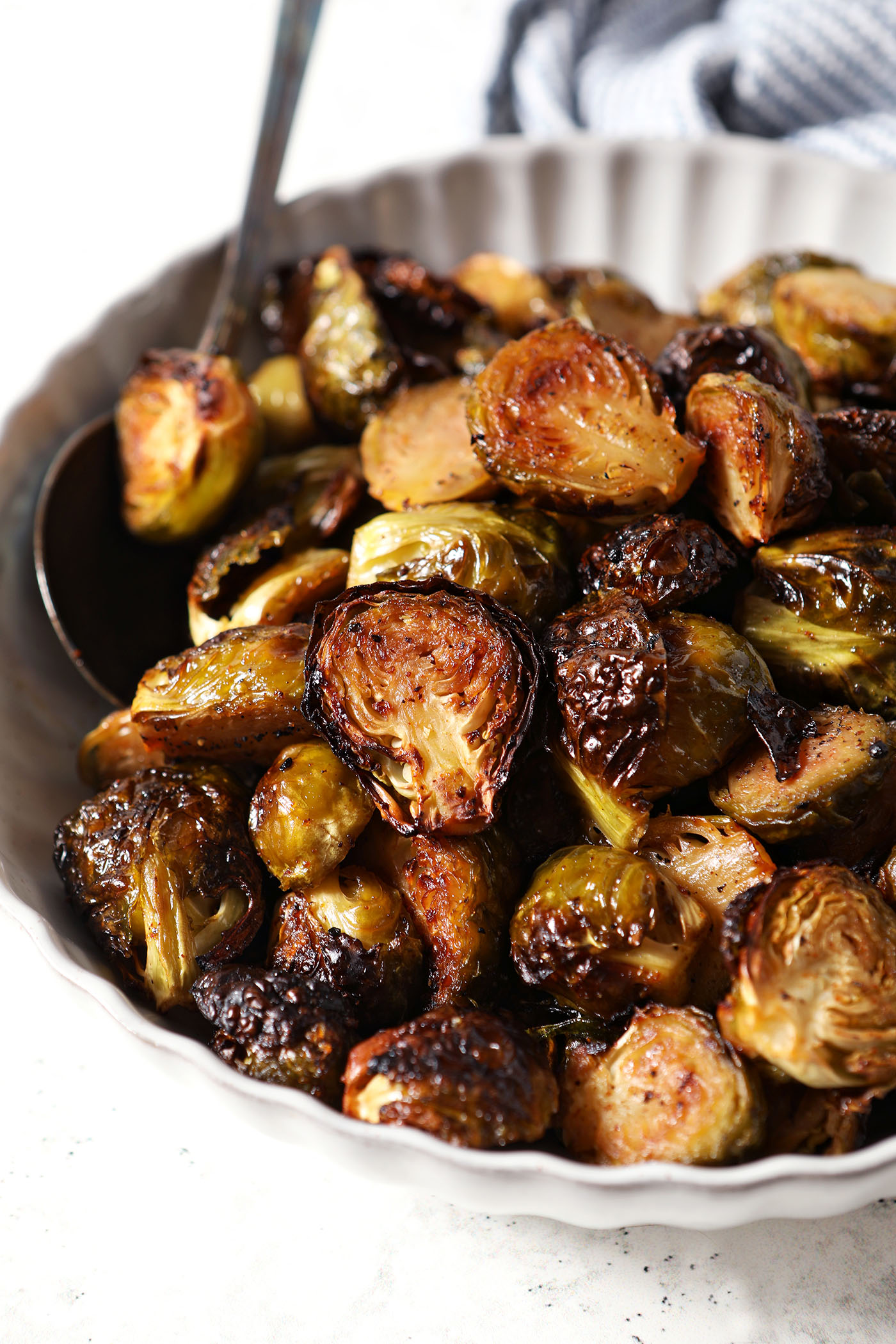 A bowl of Roasted Maple Brussels Sprouts on a white surface with a spoon in it