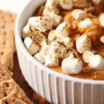 Close up of Sweet Potato Pie Dip topped with toasted marshmallows in a white bowl next to graham crackers