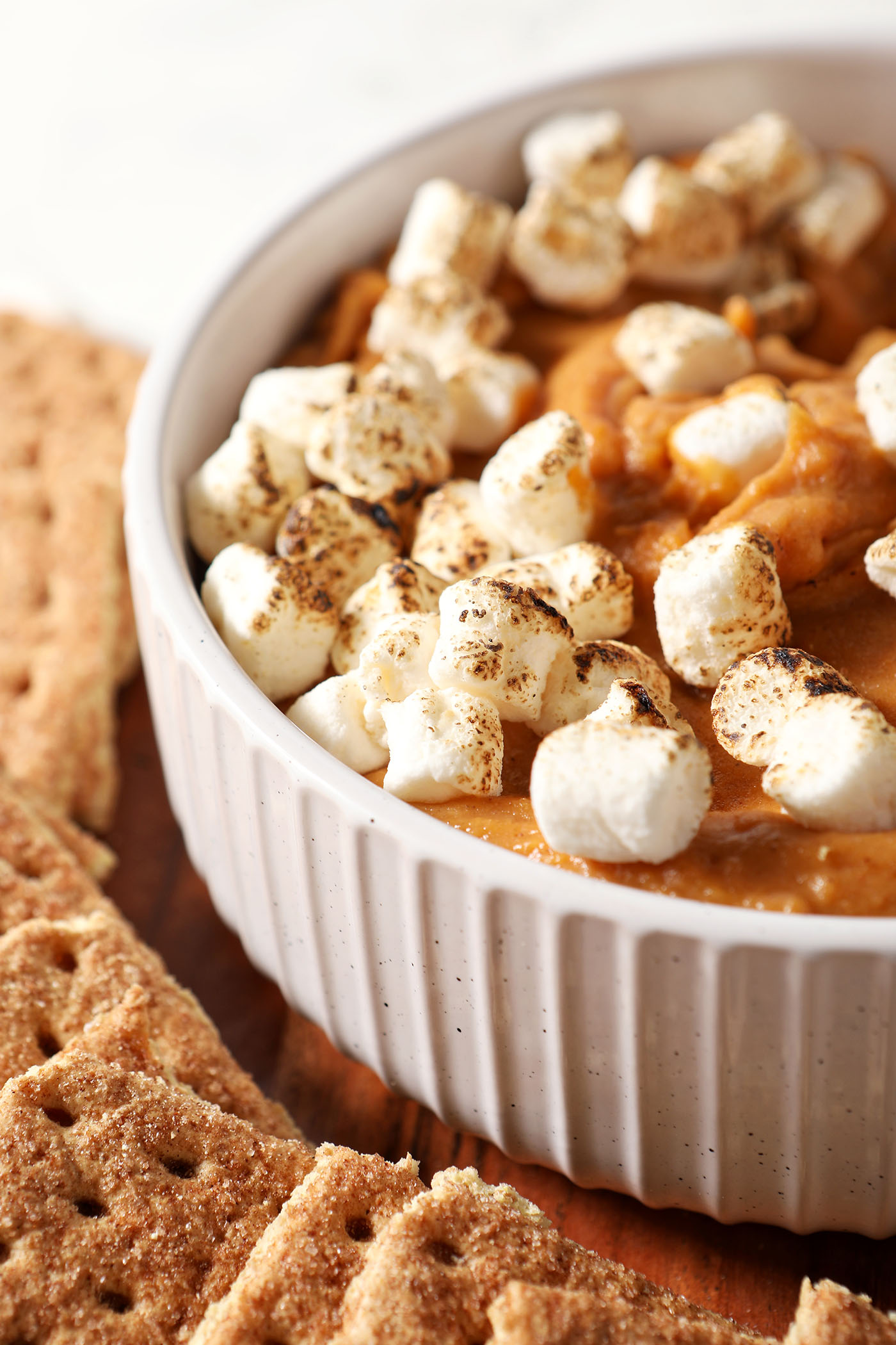 Close up of Sweet Potato Pie Dip topped with toasted marshmallows in a white bowl next to graham crackers