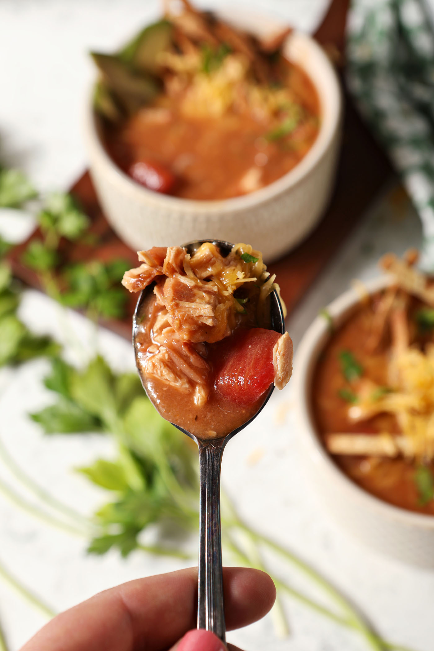 A spoon full of turkey tortilla soup above a stone surface with bowls of soup and greens