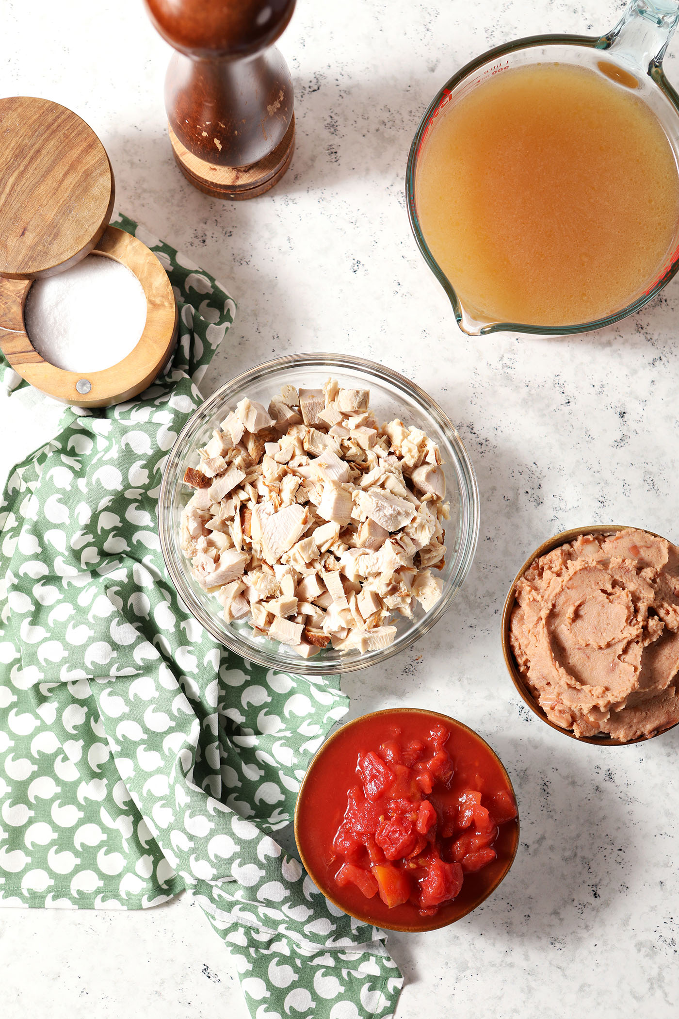 Ingredients to make easy turkey tortilla soup in bowls on a stone surface next to a green patterned linen