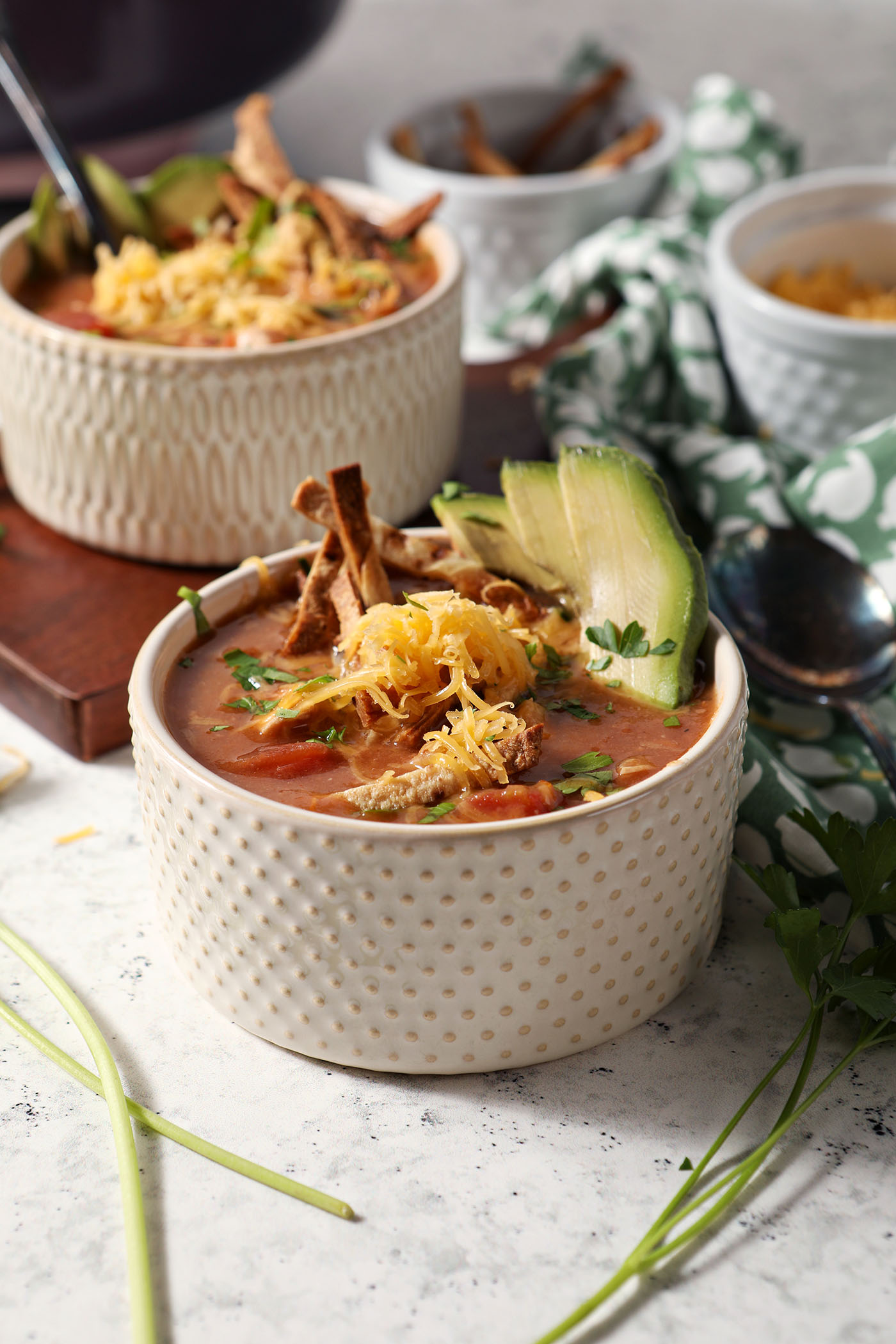 Side angle of two bowls of turkey tortilla soup garnished with tortilla slivers, avocado, cilantro and grated cheese