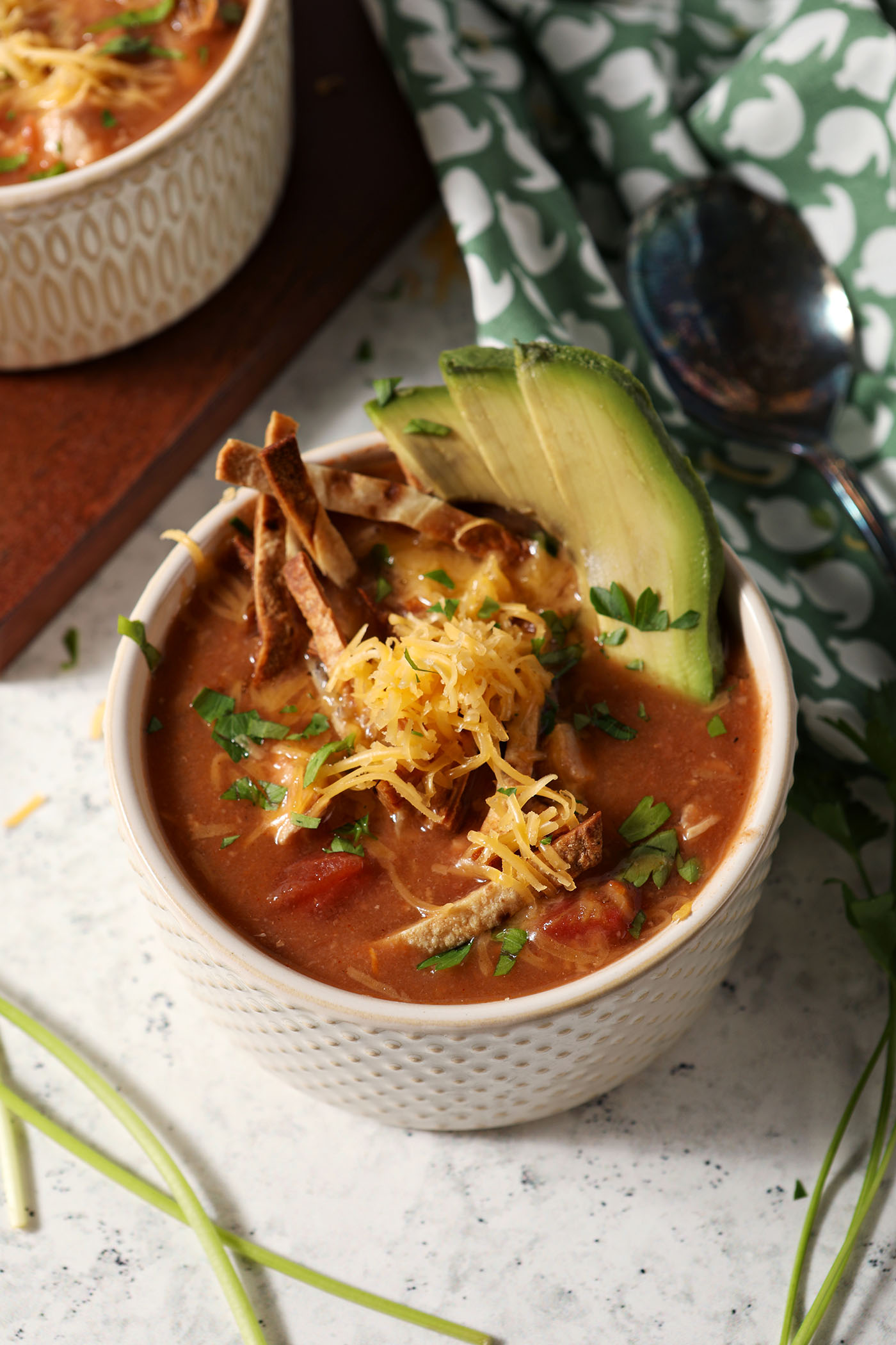Overhead of a bowl of turkey tortilla soup garnished with tortilla slivers, avocado, cilantro and grated cheese