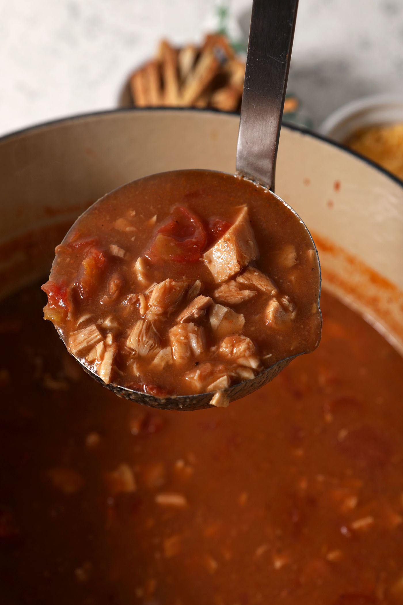 A ladle lifts a serving of turkey tortilla soup out of a dutch oven