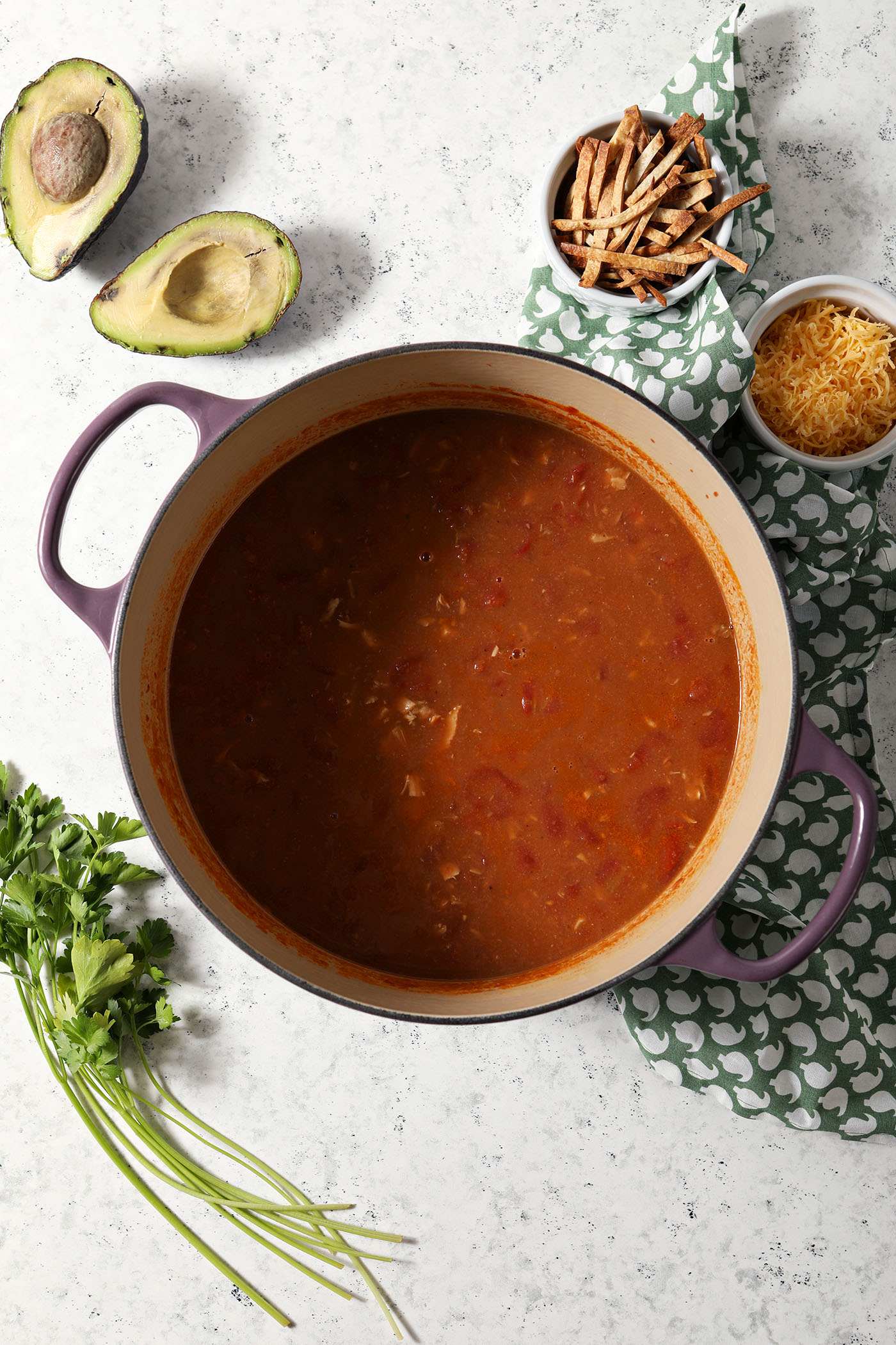 Turkey tortilla soup after cooking, on a stone surface next to garnishes for the soup