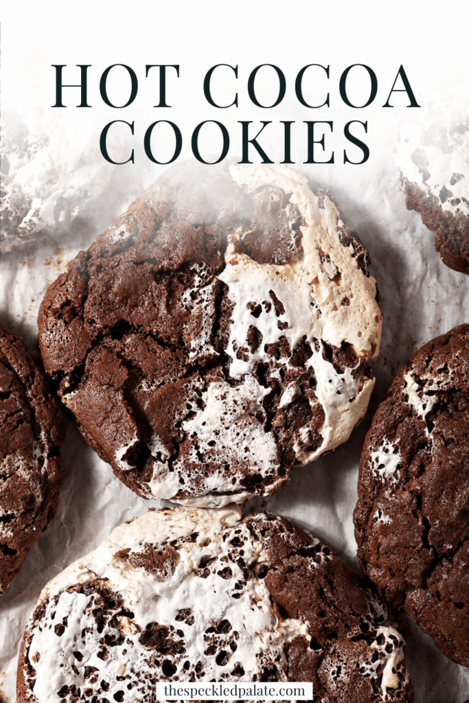 A sheet pan of baked chocolate marshmallow cookies, surrounded by marshmallows and chocolate chips with the text hot cocoa cookies