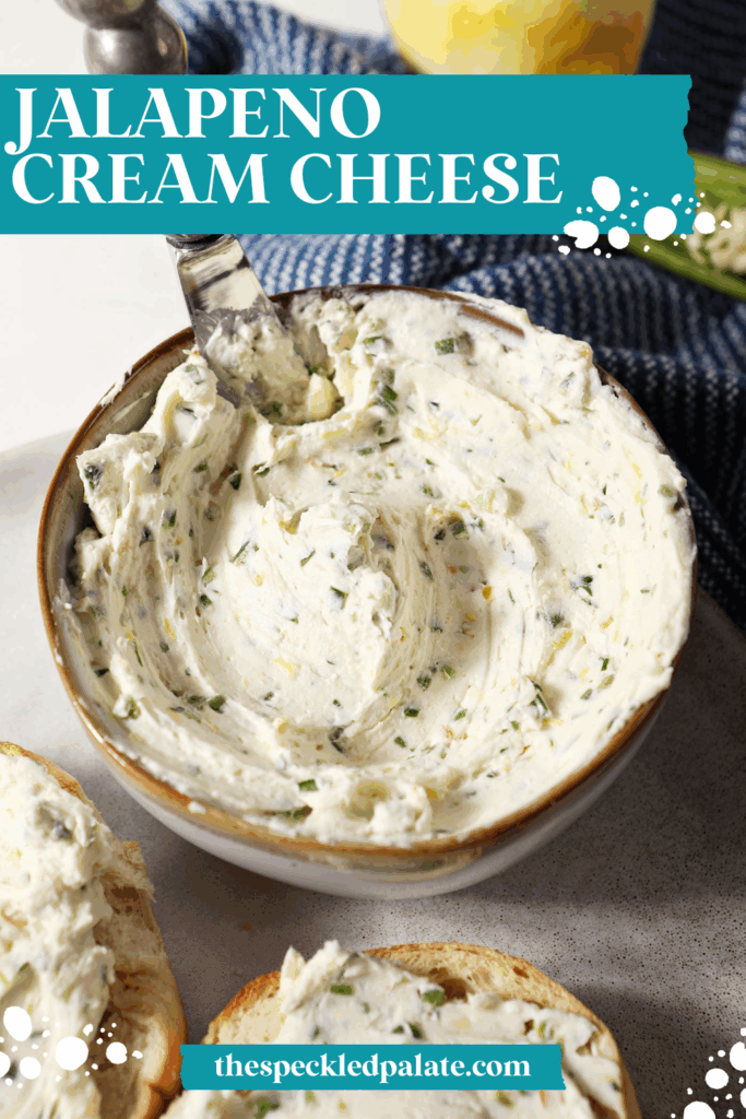 A bowl of jalapeño cream cheese on a grey plate with a knife in it on marble surface next to a blue linen with the text Jalapeno Cream Cheese