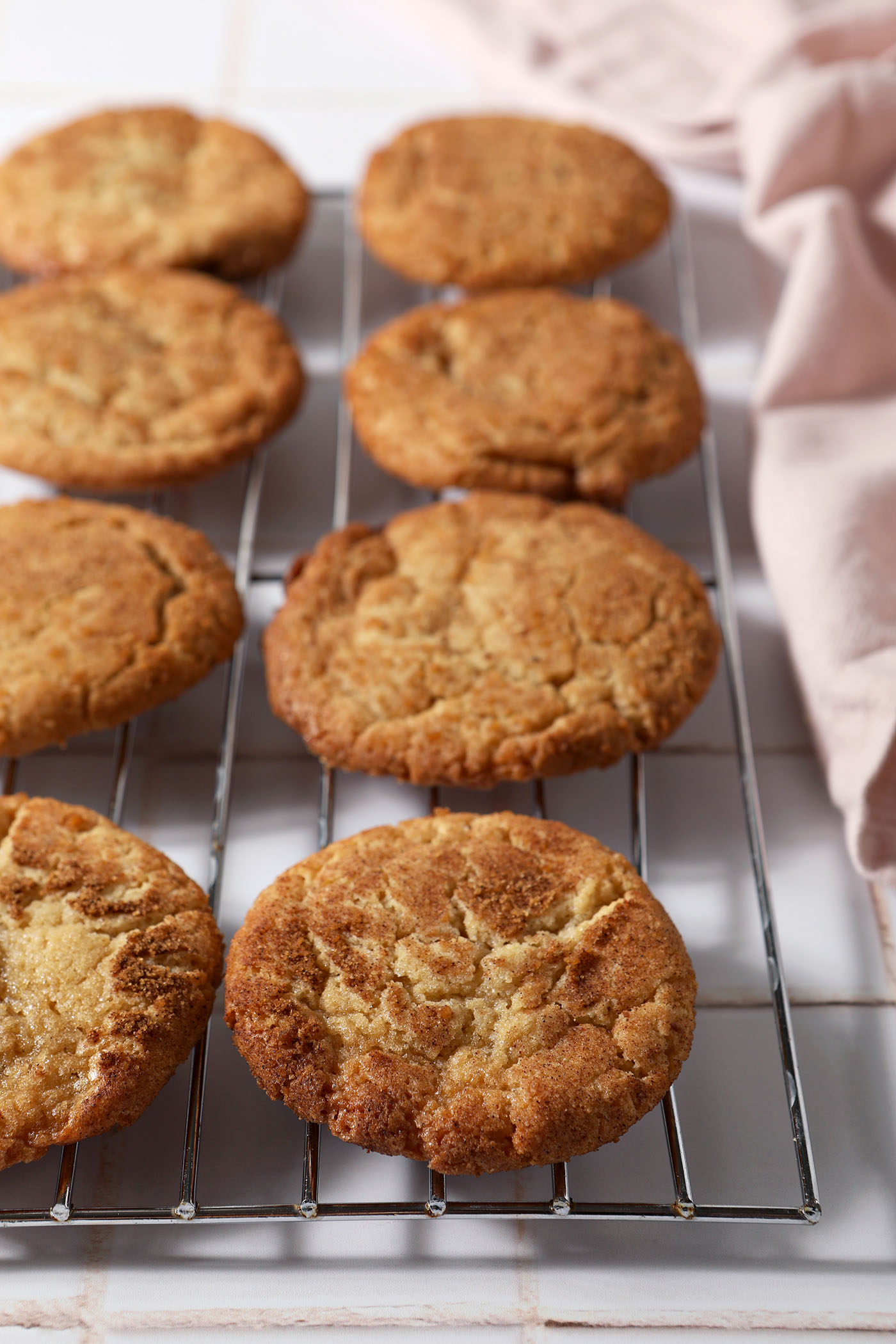 Maple cookies on a wire rack next to a pink linen after baking