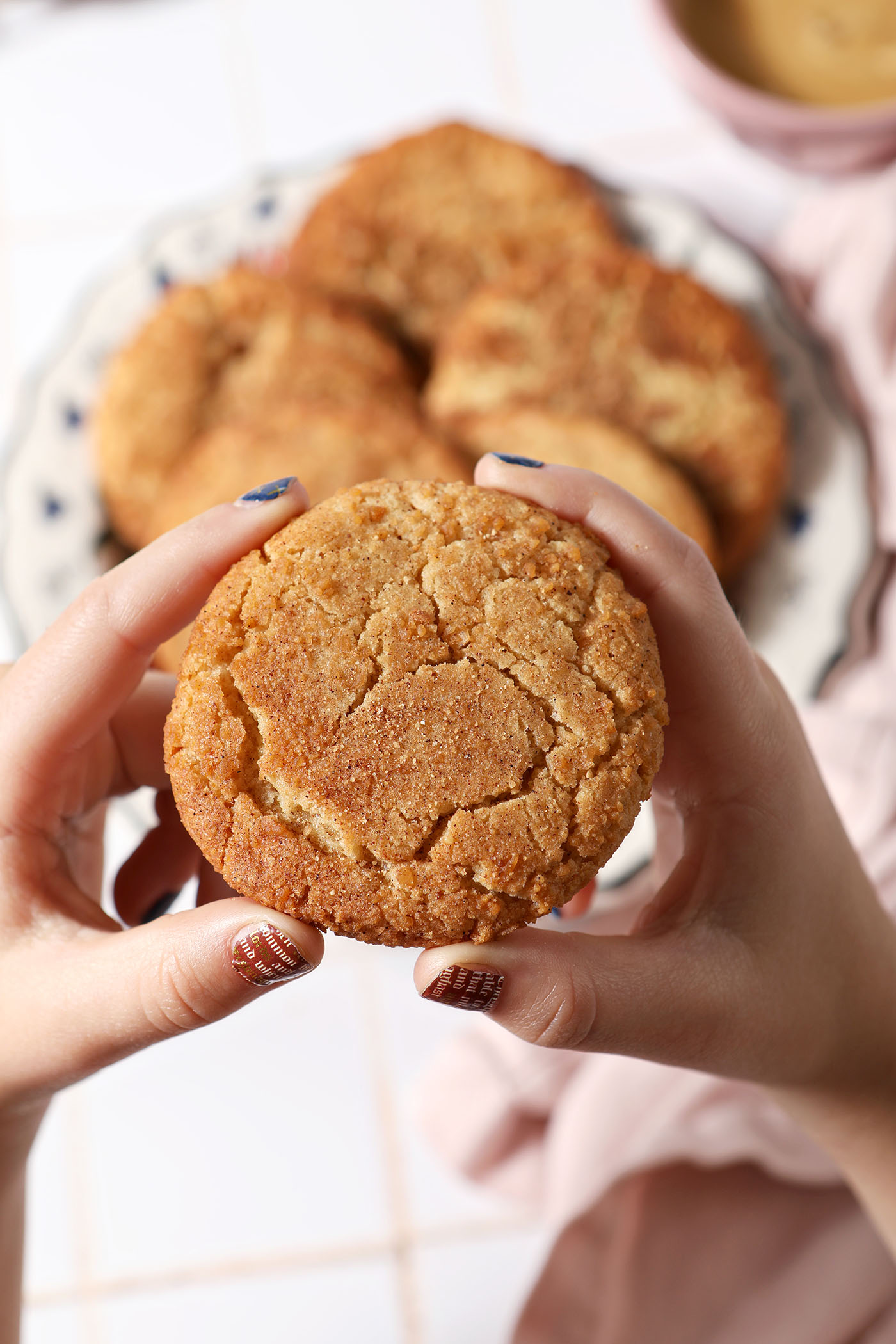 A child holds a spiced maple cookie in her hands above a platter of more cookies on a white tile surface