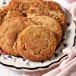 A plate of spiced maple cookies on a white tiled surface next to a pink linen