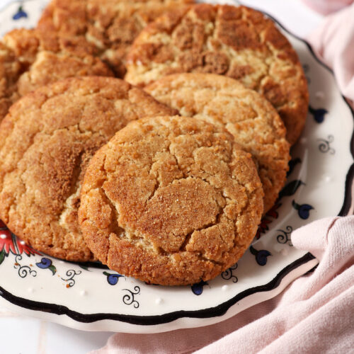 A plate of spiced maple cookies on a white tiled surface next to a pink linen