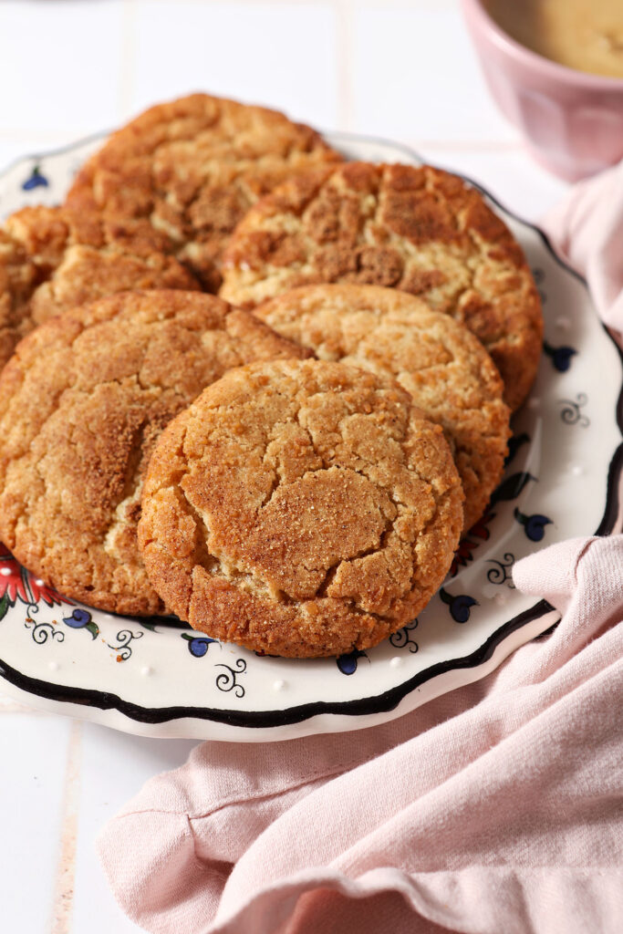 A plate of spiced maple cookies on a white tiled surface next to a pink linen