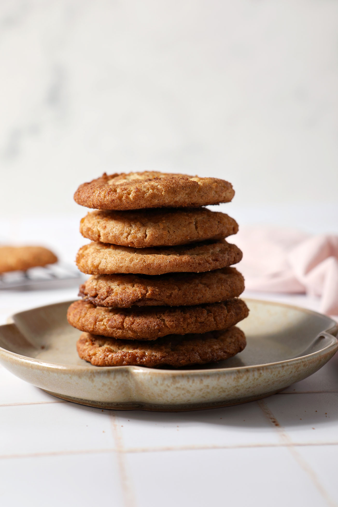 A stack of ginger cardamom maple cookies on a stoneware plate on top of a white tiled surface
