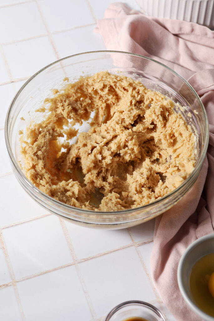 Creamed butter, sugars, ginger and maple cream in a glass bowl on a white tiled surface