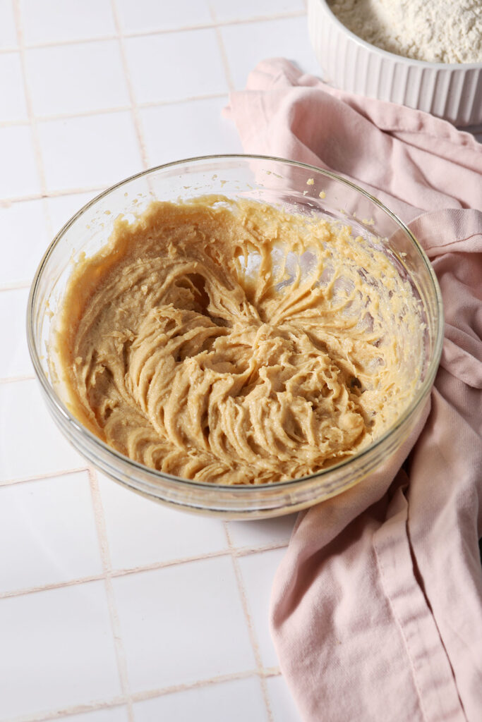 Wet ingredients for the spiced maple cookies in a bowl on a white tiled surface next to a pink linen
