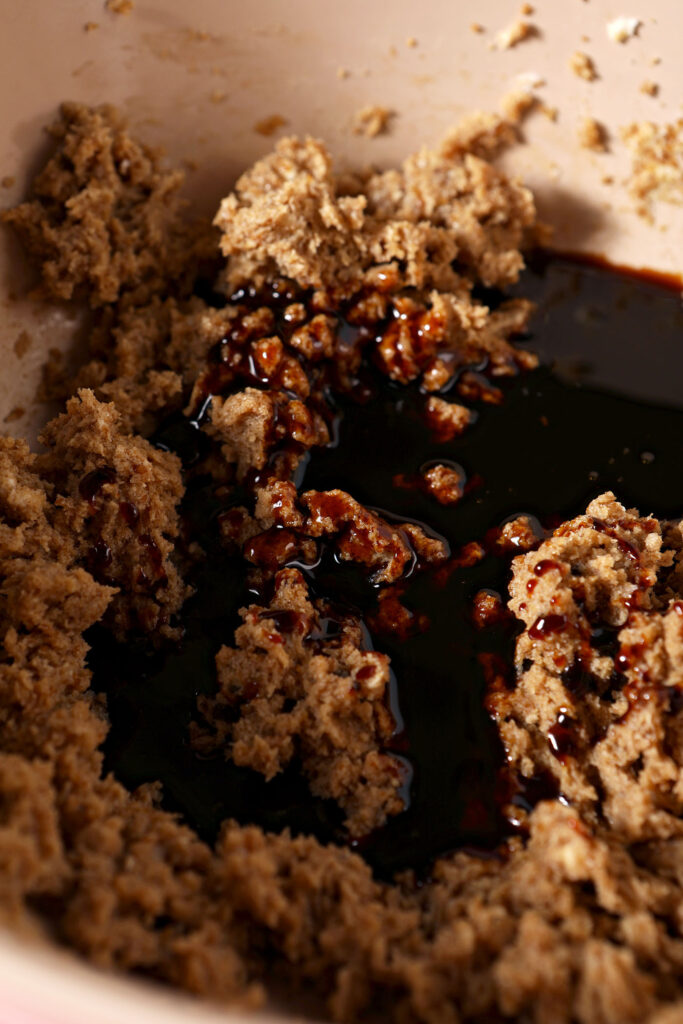 Molasses sits on top of creamed butter and sugar in a bowl before mixing
