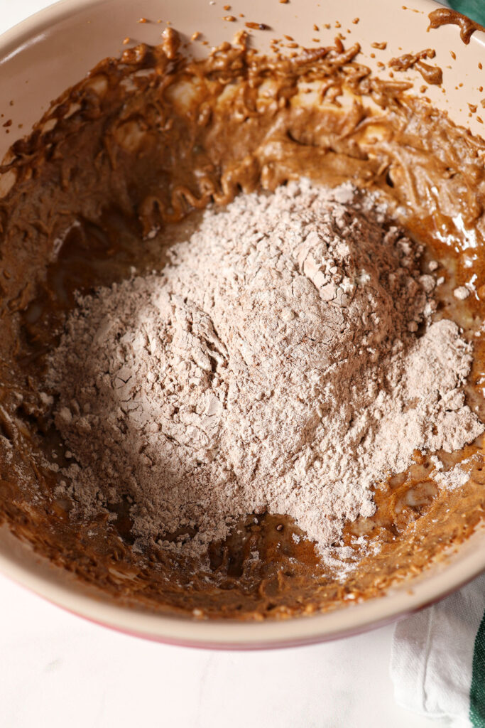 Dry ingredients sit on top of wet ingredients for chocolate ginger cookies in a bowl