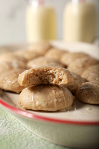 A platter of eggnog cookies with one bitten-into cookie sitting atop another on a green surface