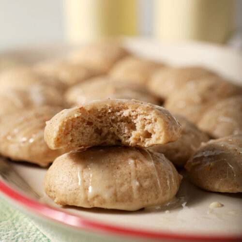 A platter of eggnog cookies with one bitten-into cookie sitting atop another on a green surface