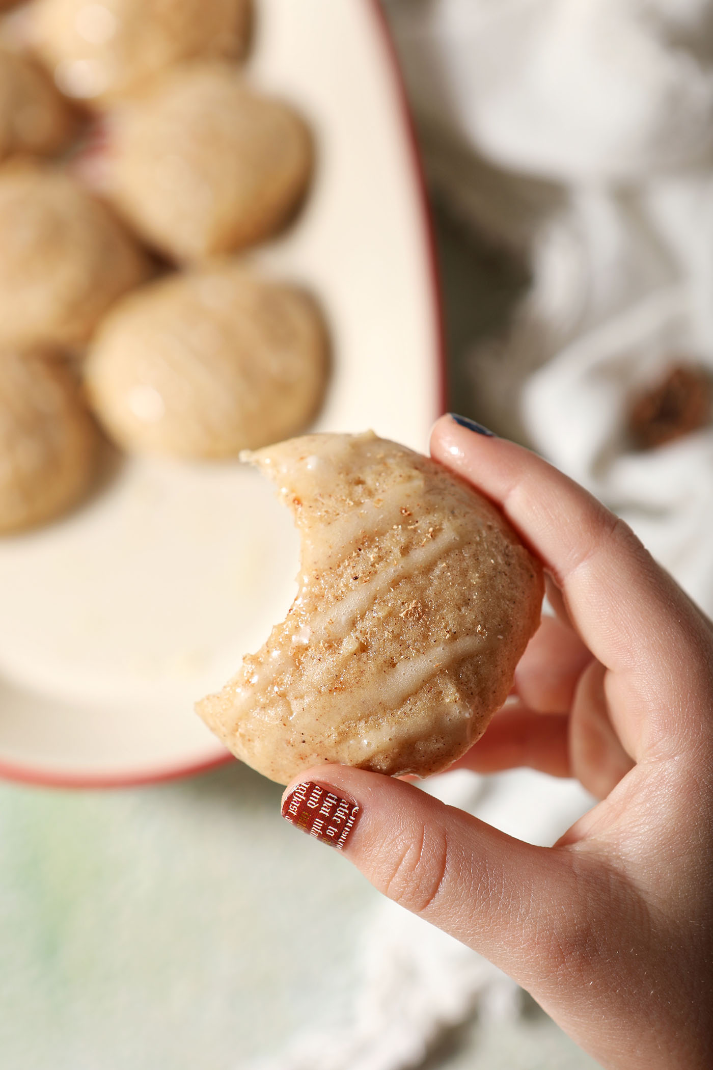 A hand holds a bitten-into eggnog cookie above a platter of more cookies on a green surface