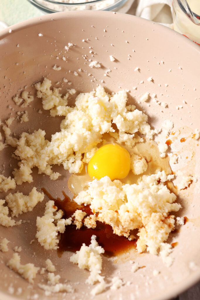 An egg and vanilla on top of creamed butter and sugar in a bowl