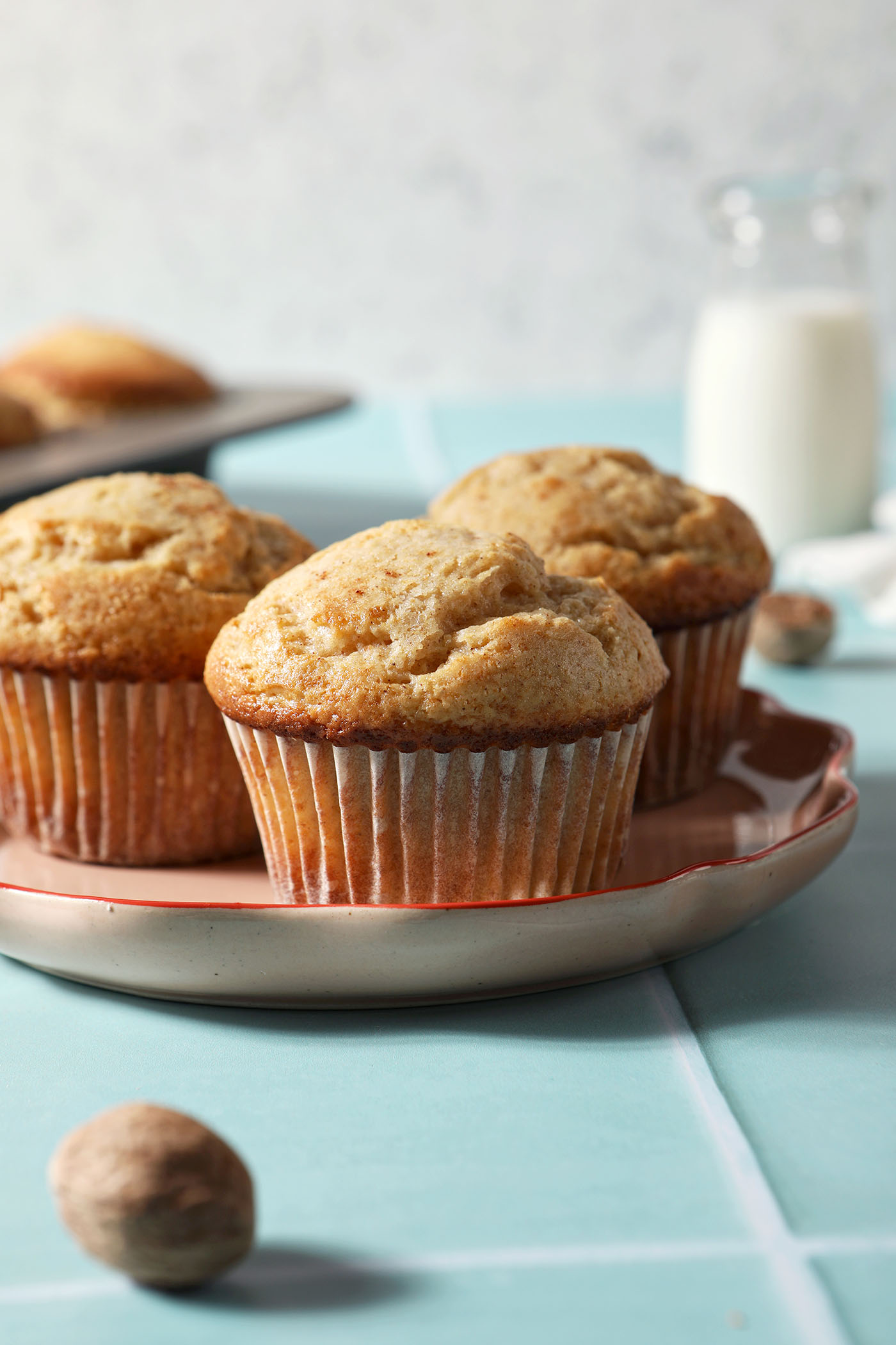 A plate of eggnog muffins on a green tiled surface in front of a muffin tin