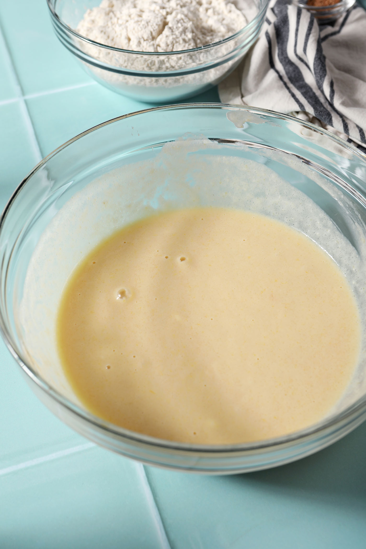 Wet ingredients in a bowl on a green tiled surface for eggnog muffins