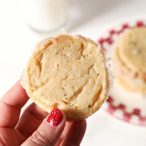 A hand holds a rosemary shortbread cookie over a plate of more cookies