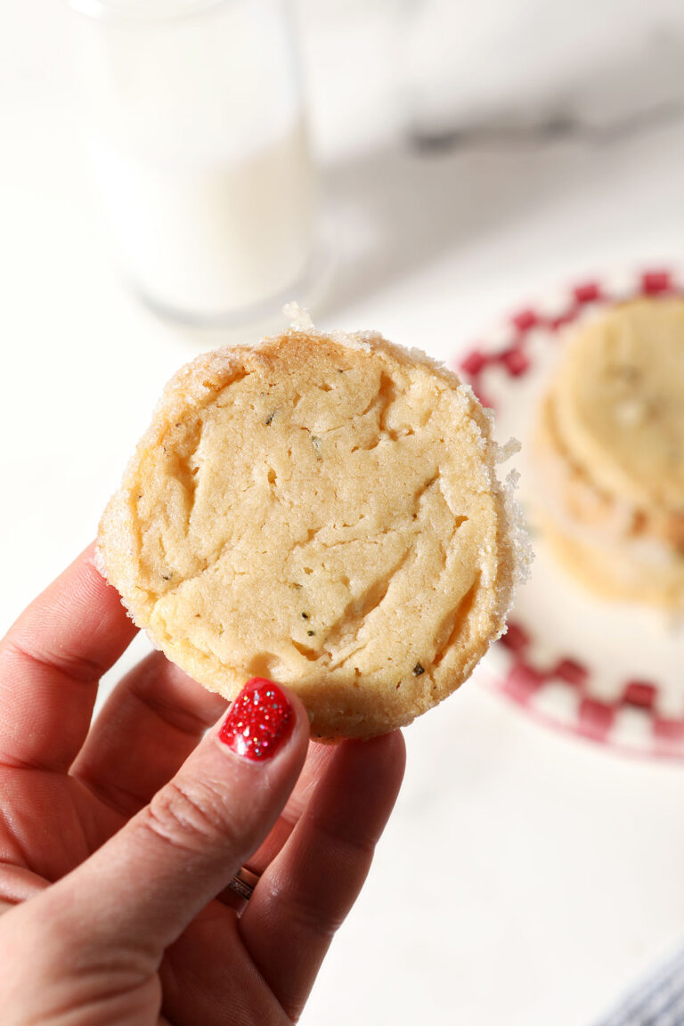 A hand holds a rosemary shortbread cookie over a plate of more cookies