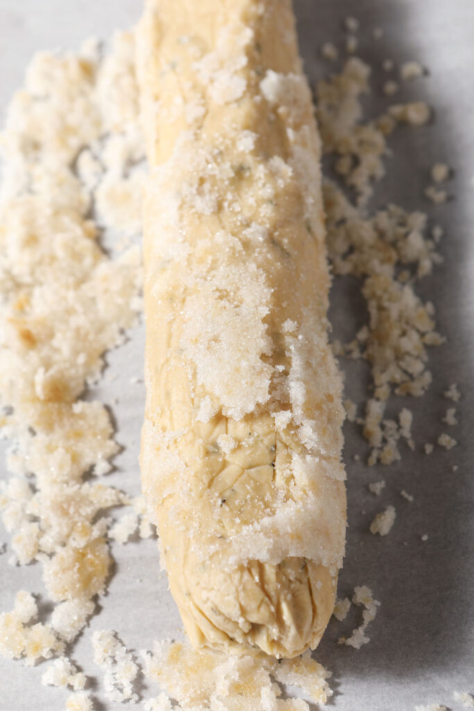 A log of shortbread on top of ginger sugar on a piece of parchment