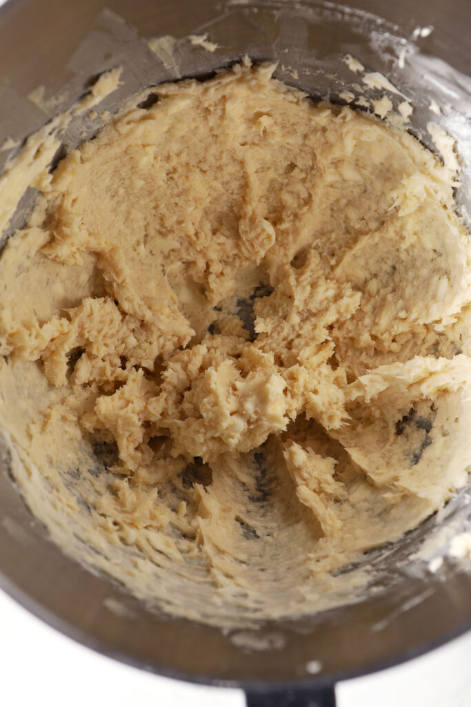 Two sticks of butter with powdered sugar and maple syrup in the metal bowl of a stand mixer before creaming