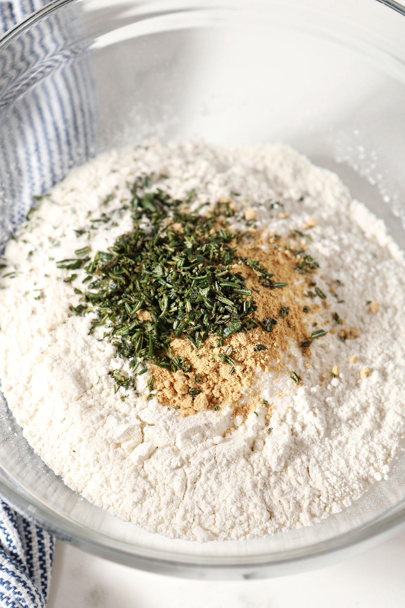 Dry ingredients for rosemary ginger shortbread in a glass bowl on a white stone surface