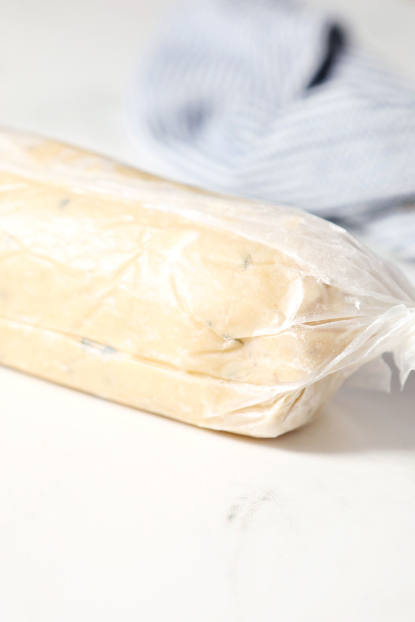 Shortbread cookie dough rolled into a log shape in plastic wrap on a white stone surface