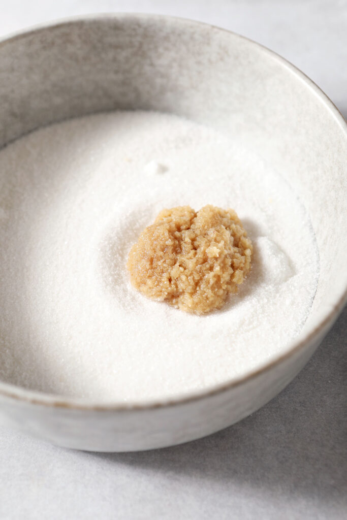 Fresh ginger on top of granulated sugar in a grey bowl