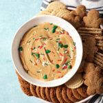 A bowl of gingerbread dip next to cookies and crackers on a teal surface