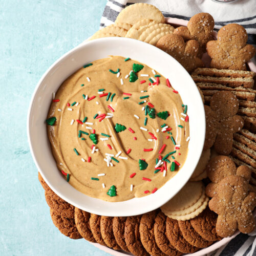 A bowl of gingerbread dip next to cookies and crackers on a teal surface