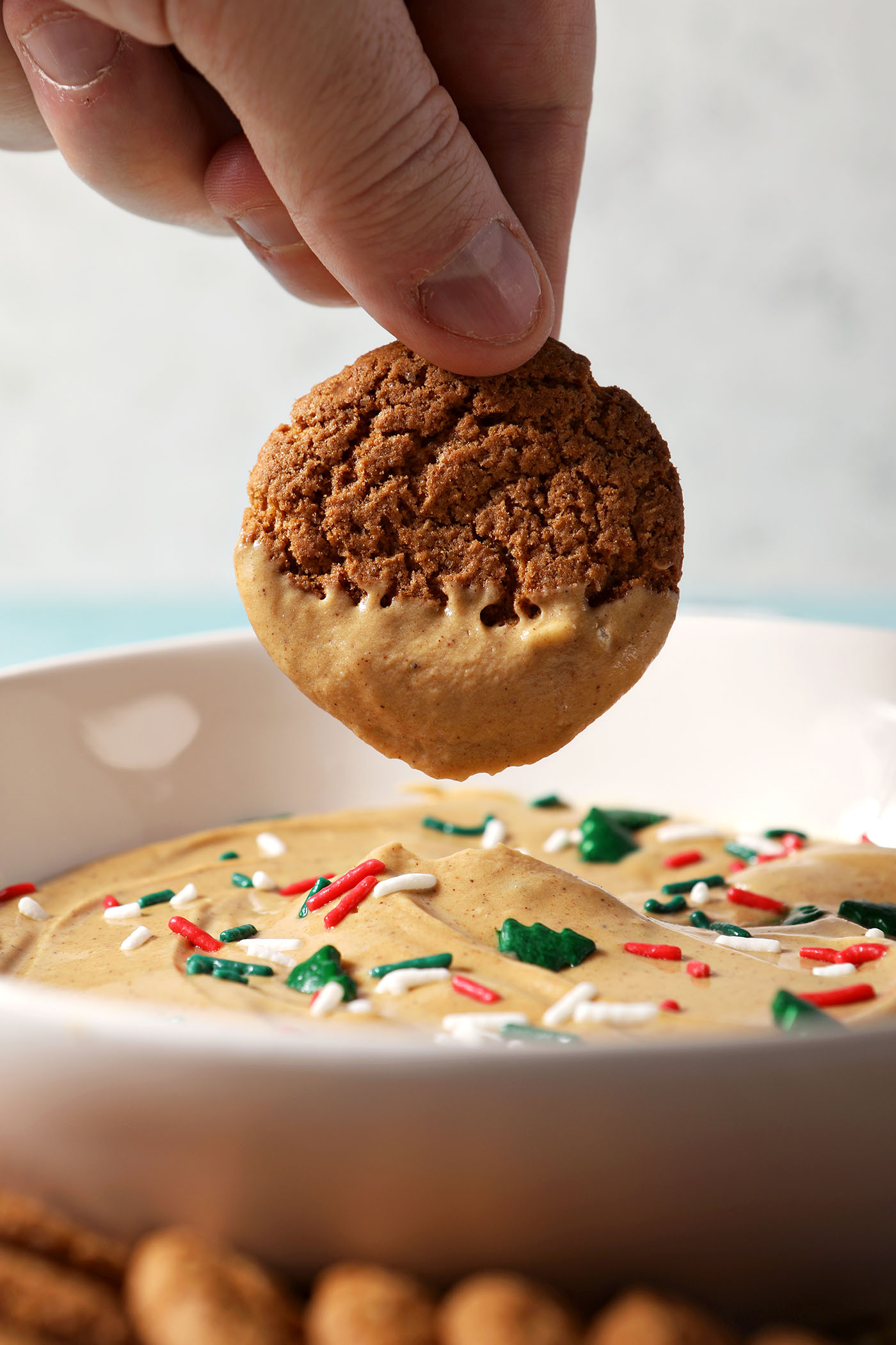 A hand dips a gingersnap into a bowl of gingerbread dip