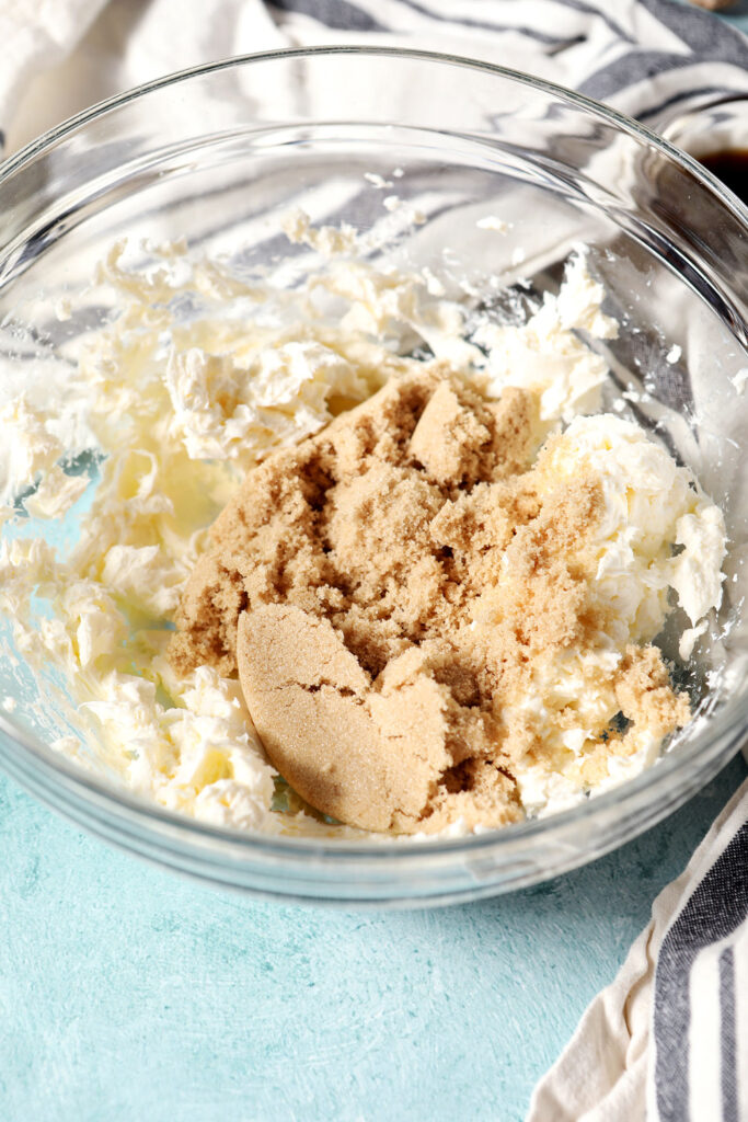 Brown sugar on top of whipped cream cheese in a glass bowl on a teal surface