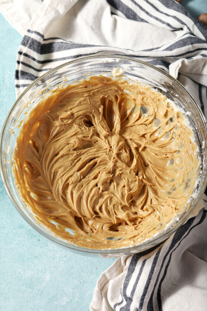 Whipped cream cheese gingerbread dip in a bowl on a teal surface surrounded by a black and white striped linen