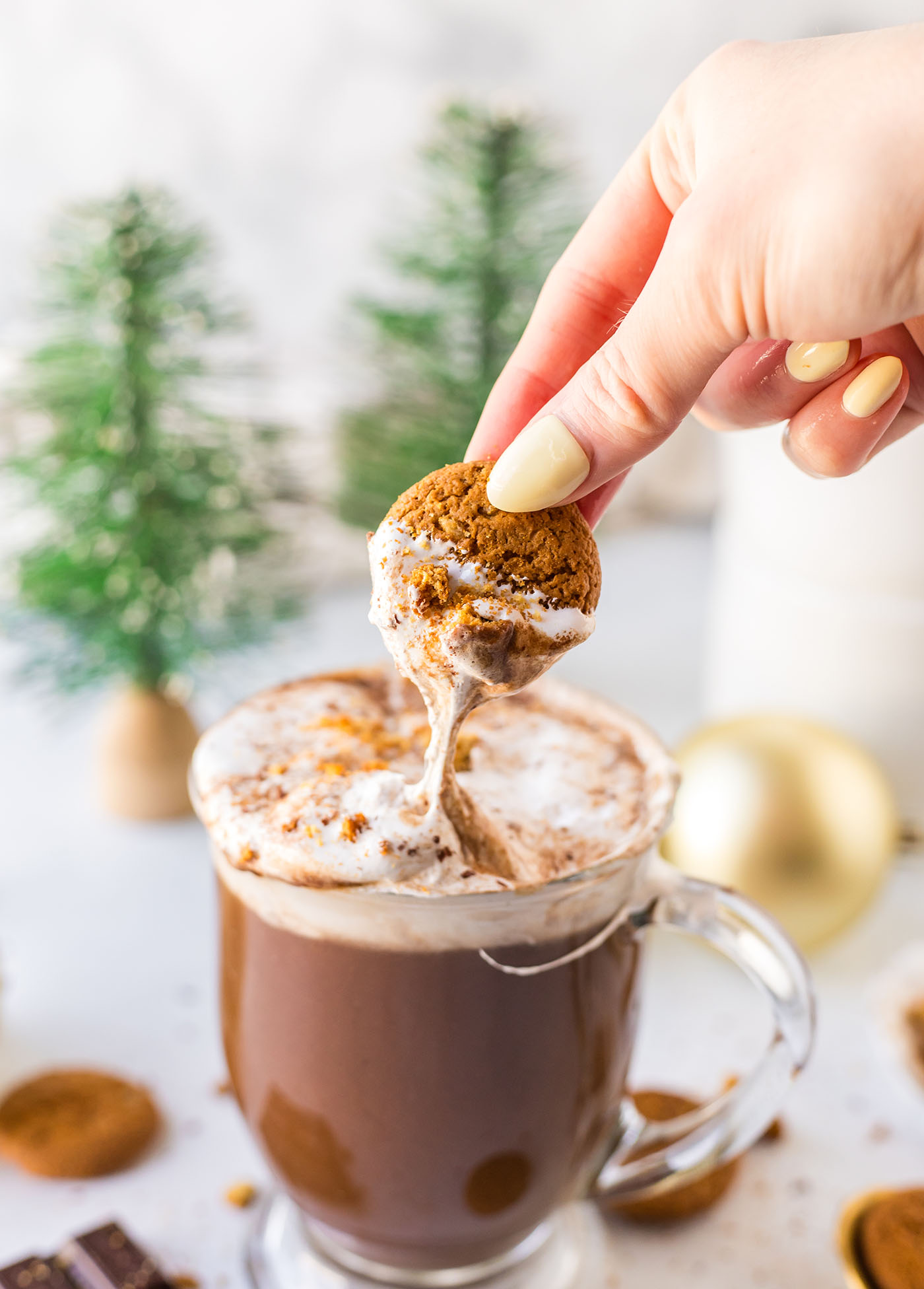 a hand pulls a cookie coated in marshmallow fluff from a mug of cocoa