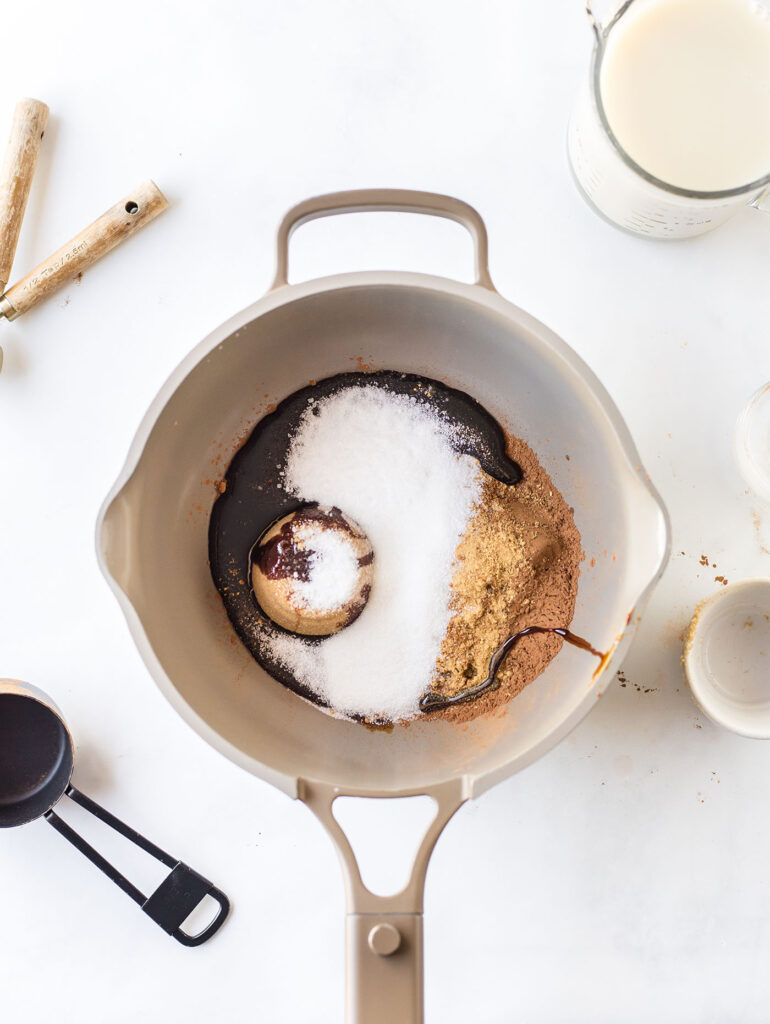 A saucepan full of ingredients to make gingerbread hot chocolate before heating on a white surface