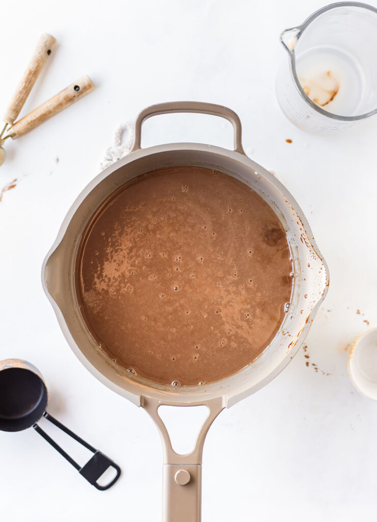 Gingerbread hot chocolate in a saucepan after the milk is added, but before it’s thickened up on a white surface