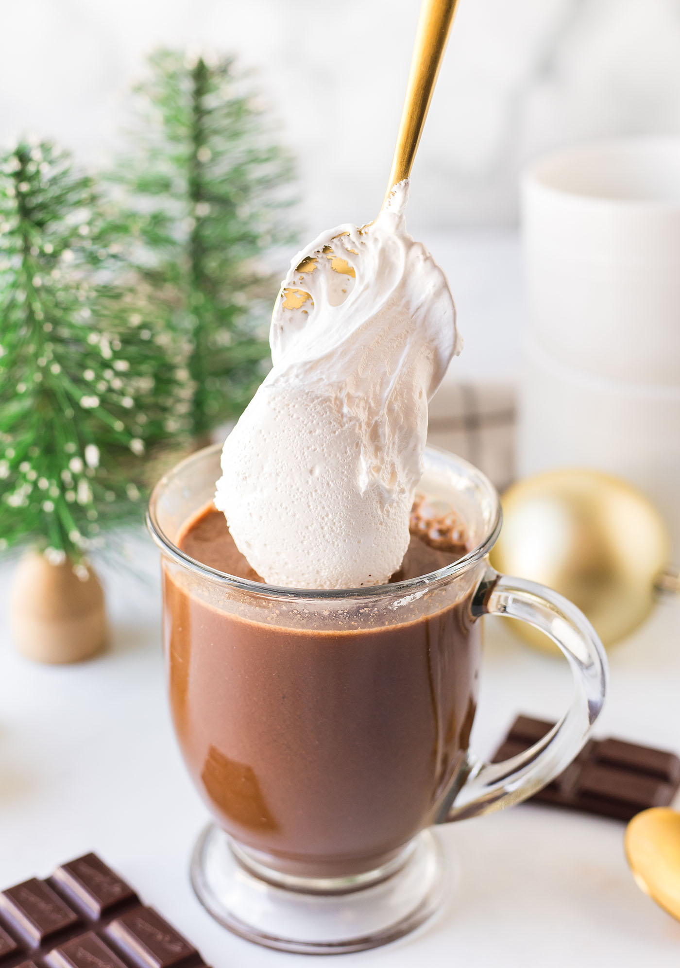 A spoon scoops marshmallow fluff of top of a mug of hot cocoa