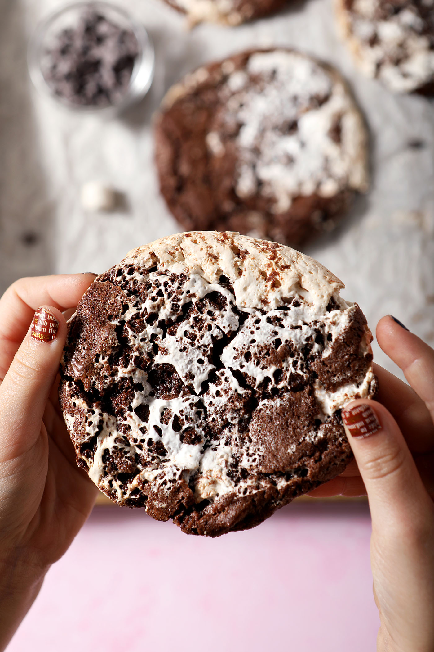 A child holds a large hot chocolate cookie between their hands above a sheet pan of more cookies