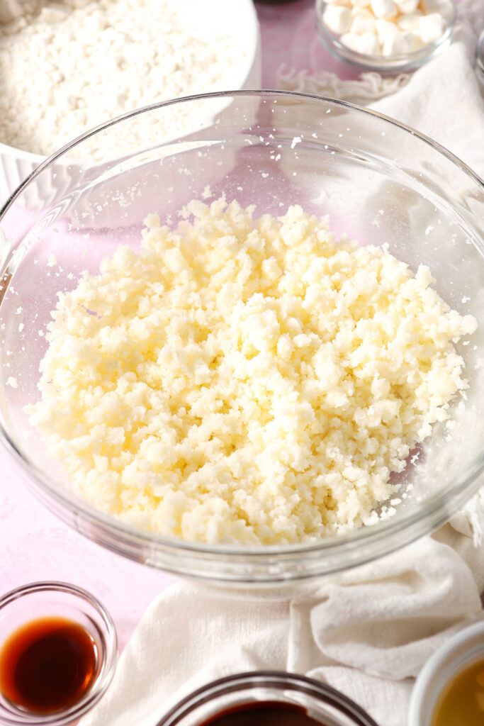 Creamed butter and sugar in a bowl on a pink surface, surrounded by other cookie ingredients