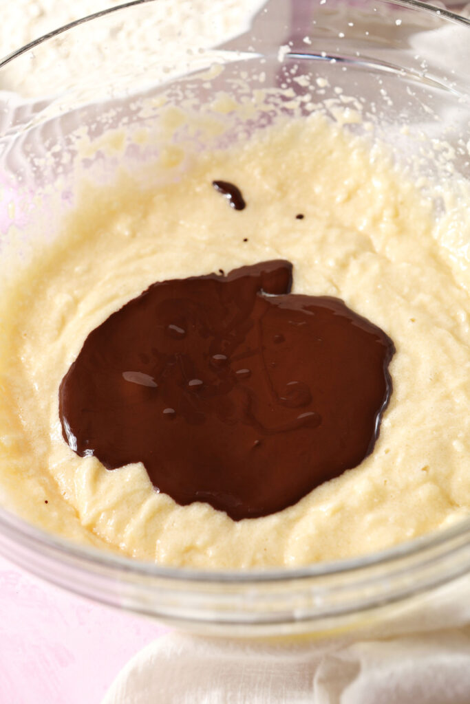 Melted chocolate sits on top of other wet ingredients in a bowl before mixing